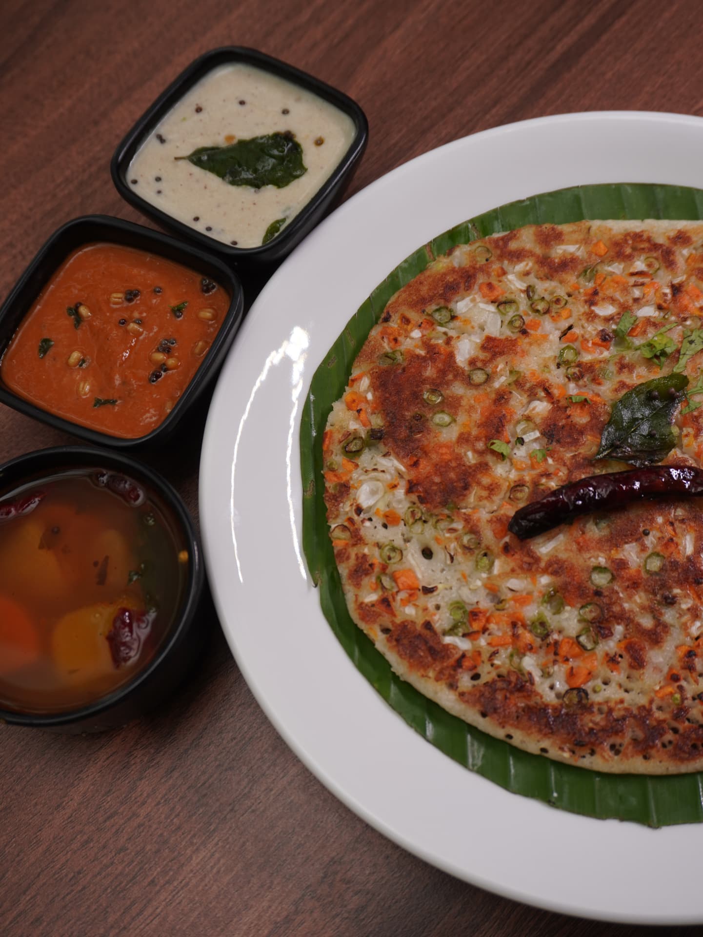 Vegetable uttapam on banana leaf with chutneys and sambar